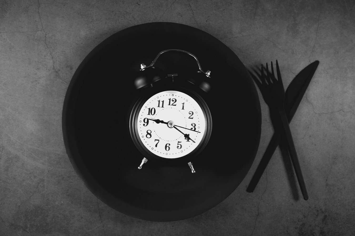 Alarm clock on a plate with cutlery, representing a timed fast