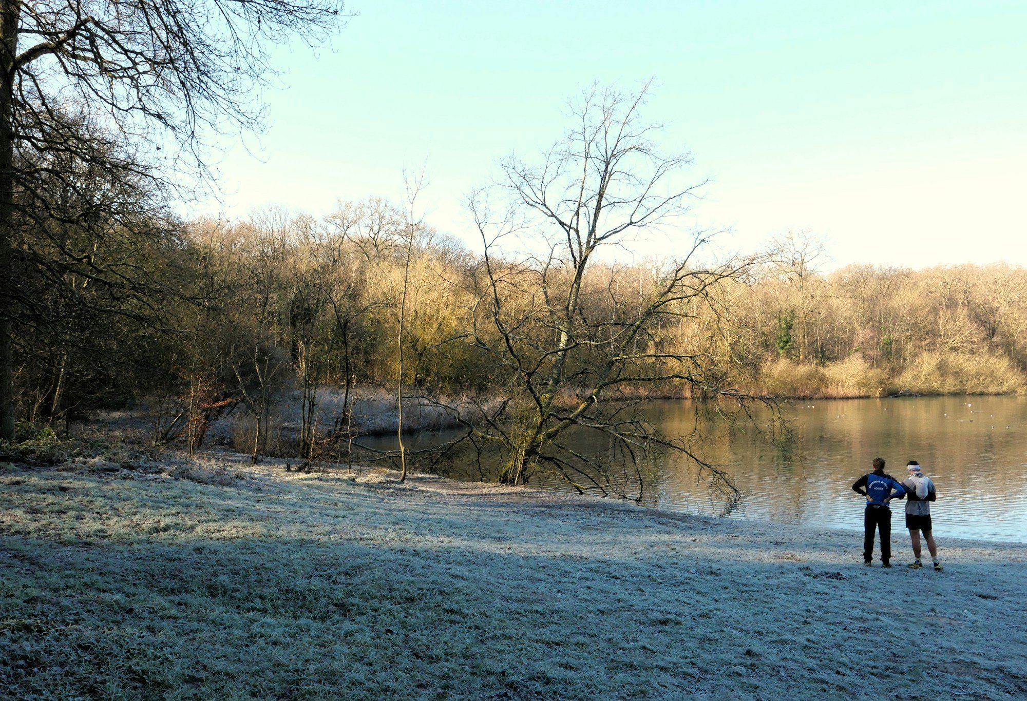 Two people standing near a frosty lakeshore in winter