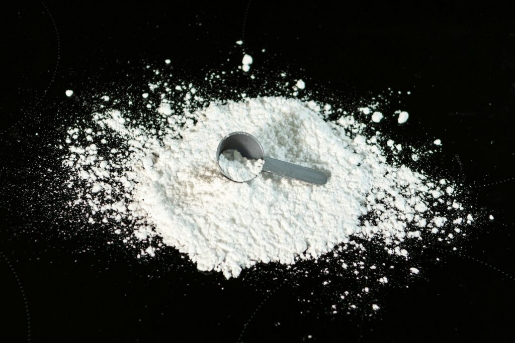 Creatine powder with a measuring scoop on a dark surface
