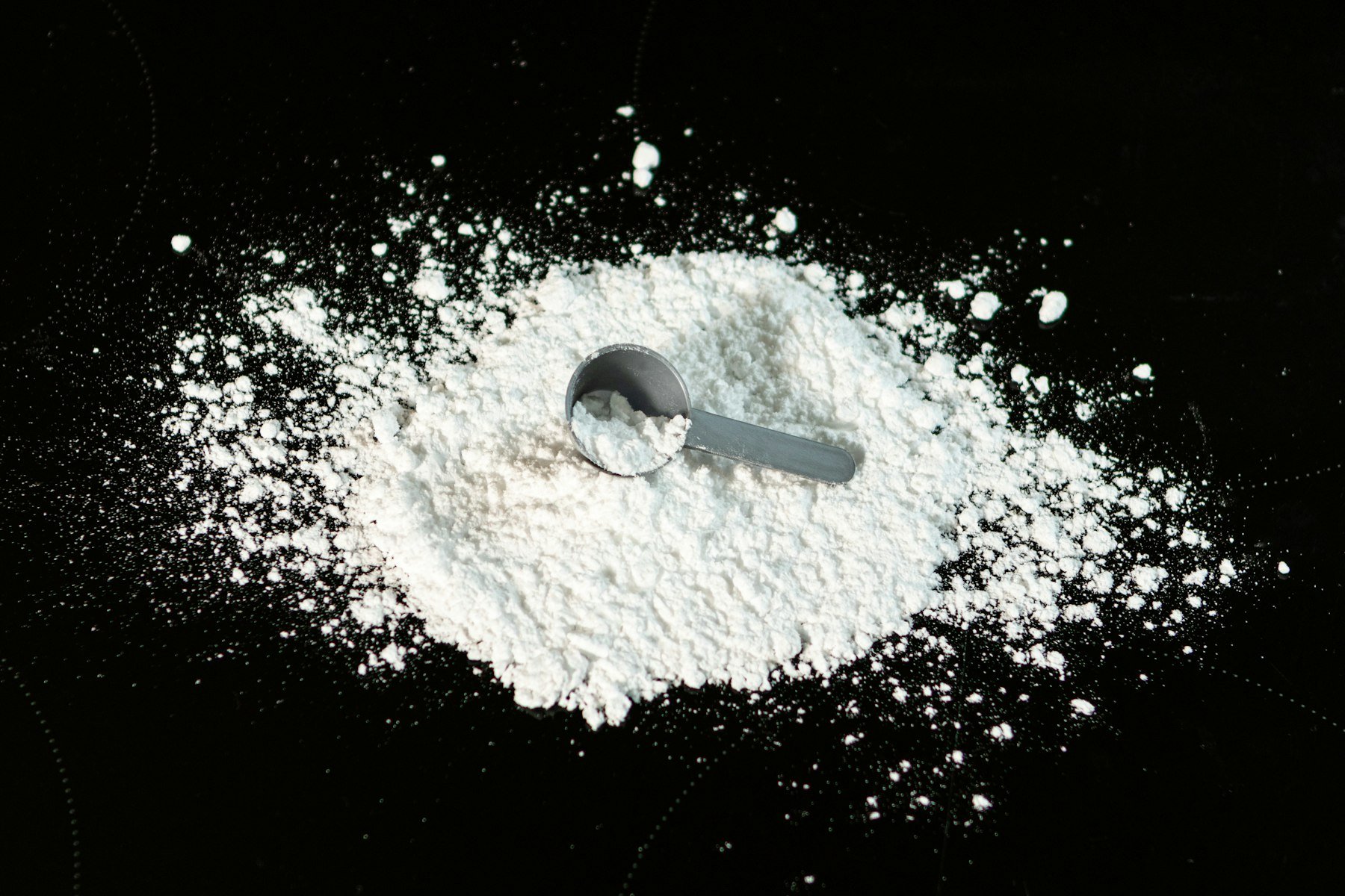 Creatine powder with a measuring scoop on a dark surface