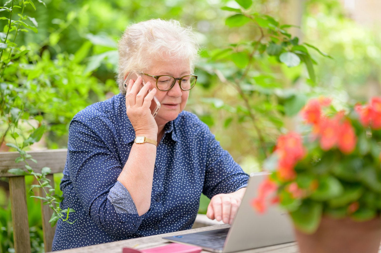 Older woman using a laptop outdoors while on the phone