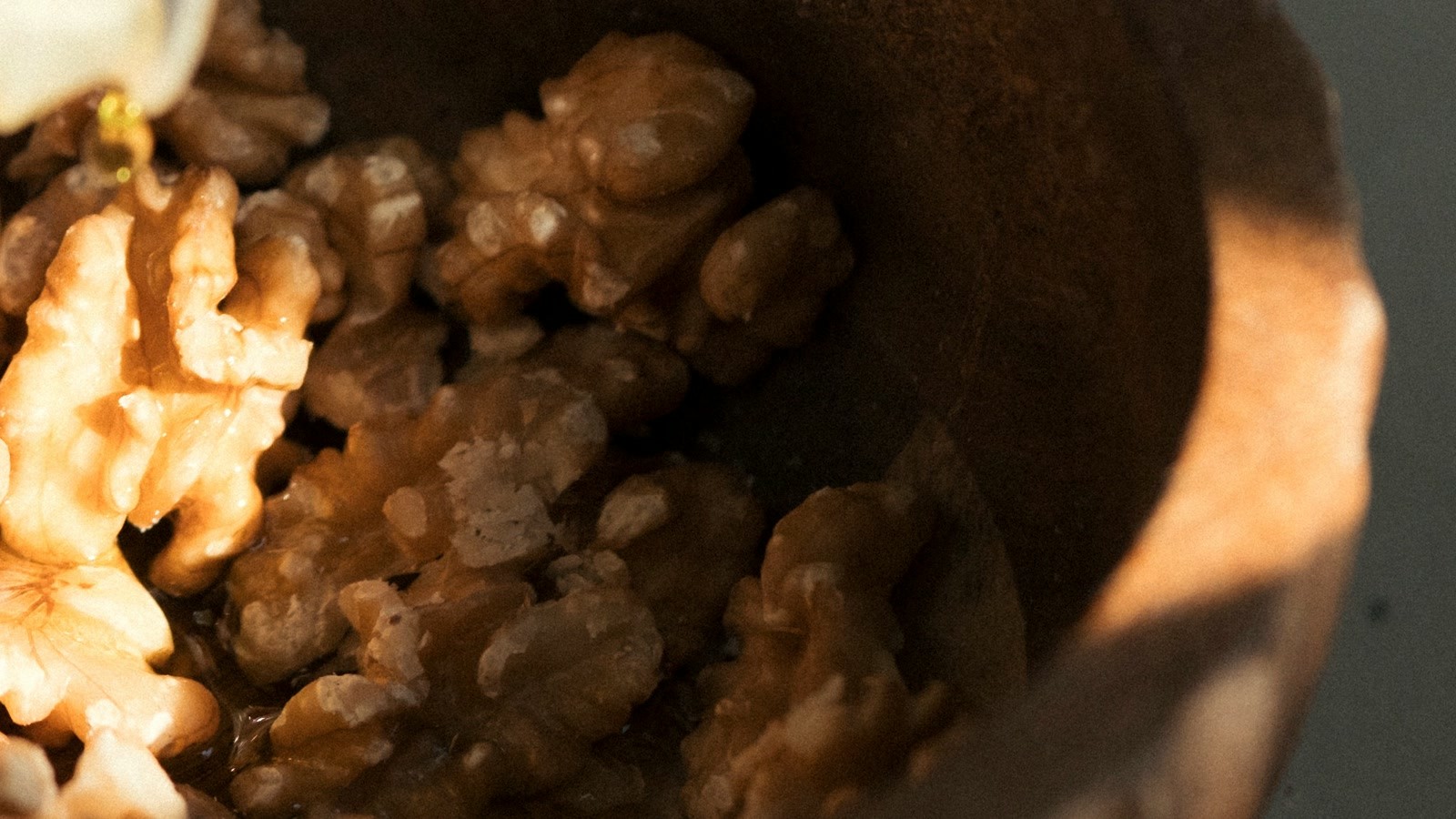Olive oil being poured over walnuts in a wooden bowl