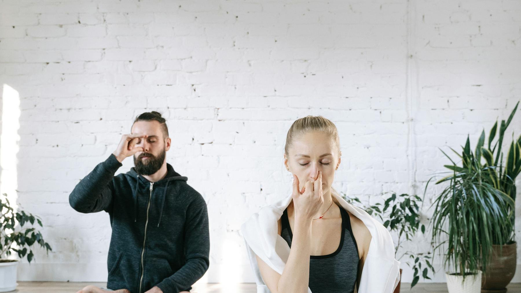Two people practising breathing exercises indoors on yoga mats