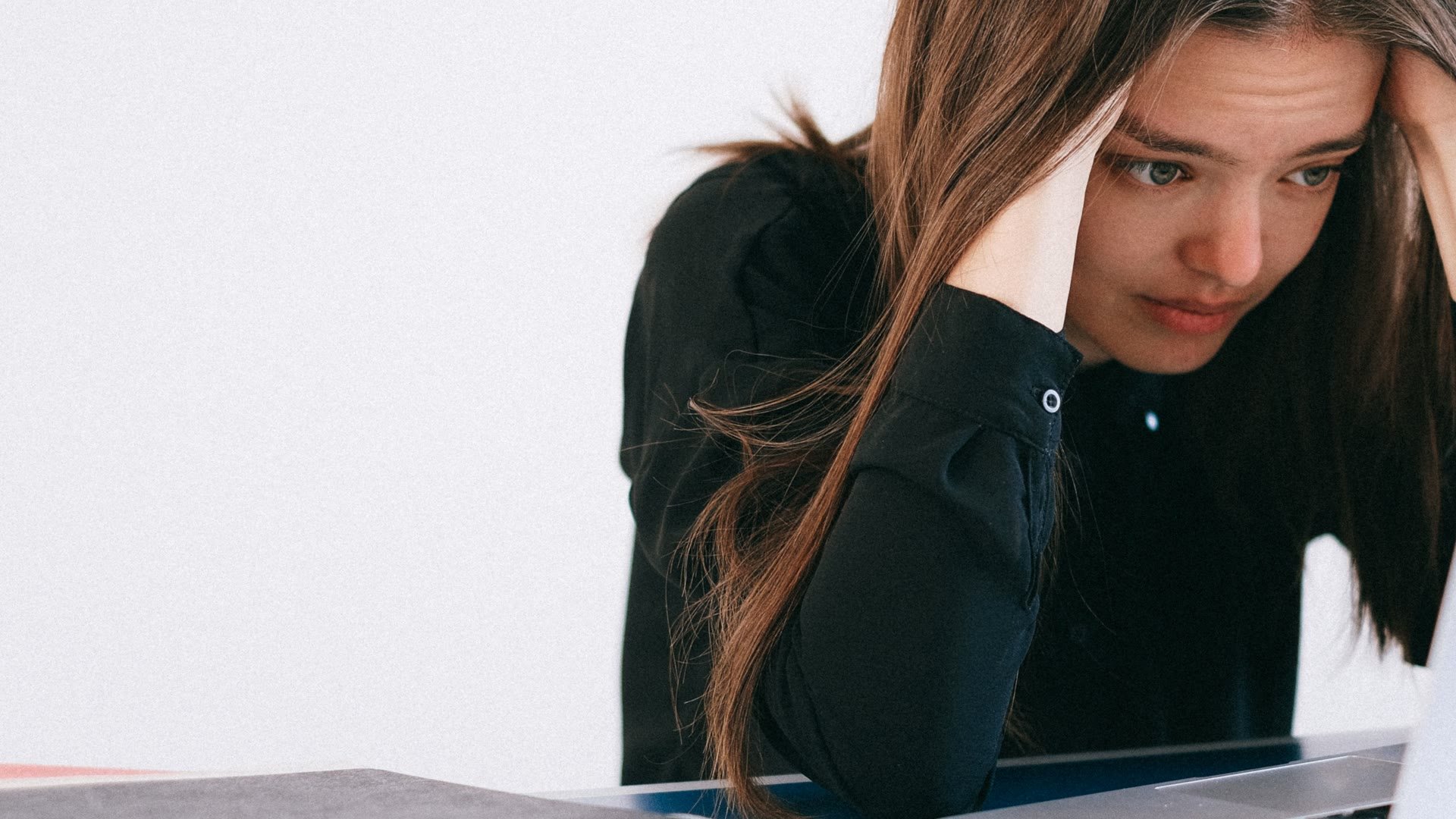 A stressed woman leaning over a laptop at a desk