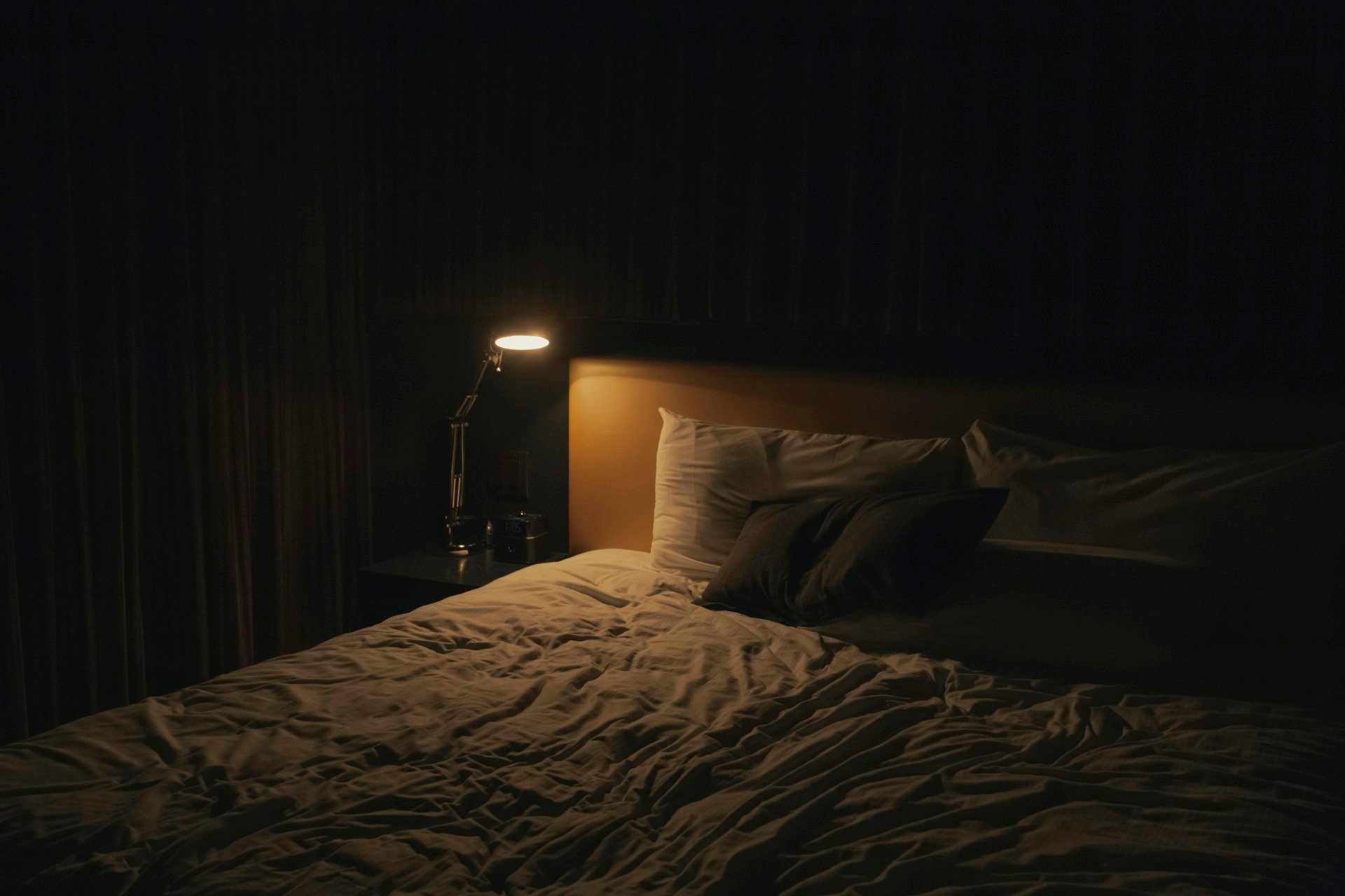 Table lamp turned on beside a bed in a dim bedroom