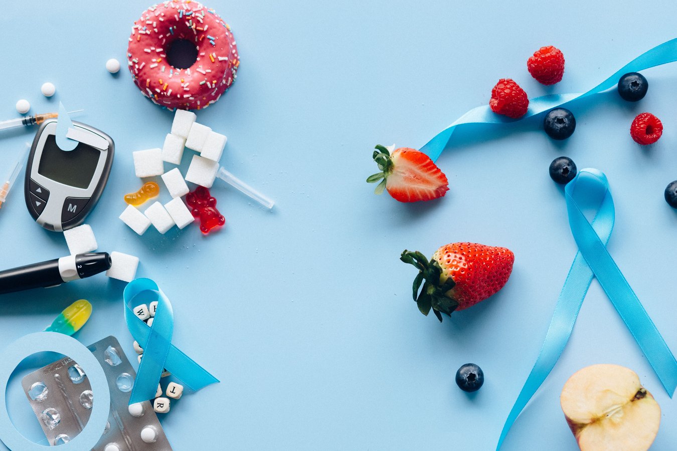 A glucose meter with fruit and sugar cubes on a blue background