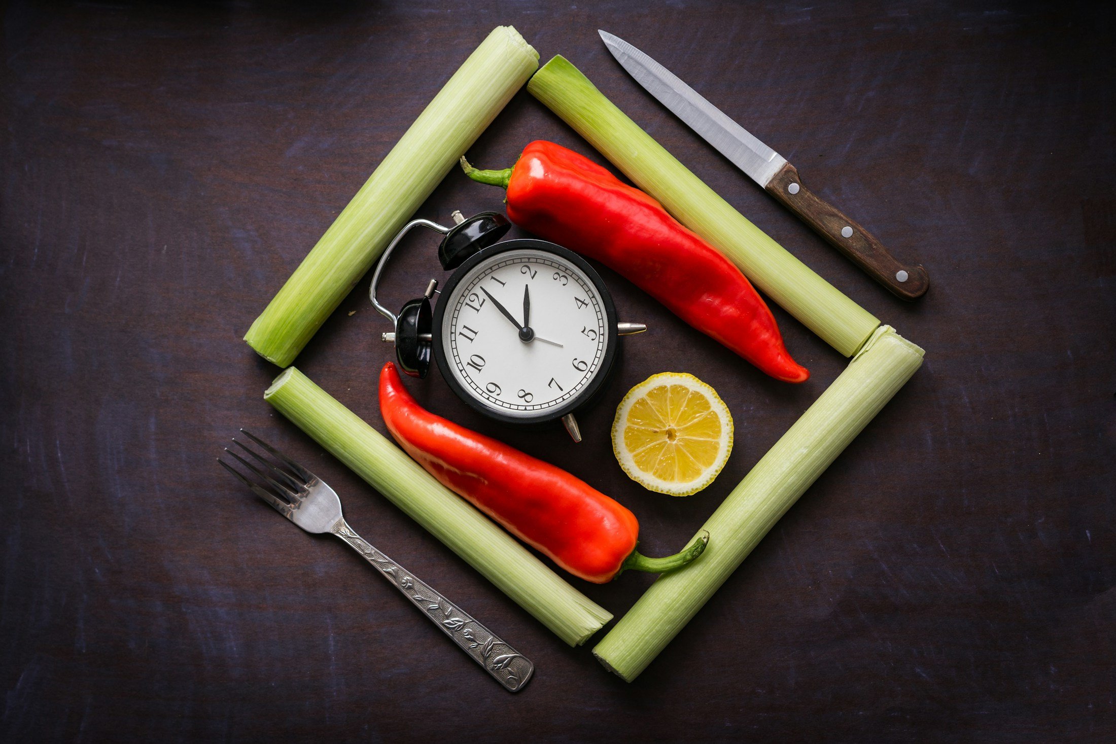 A clock surrounded by vegetables and a knife