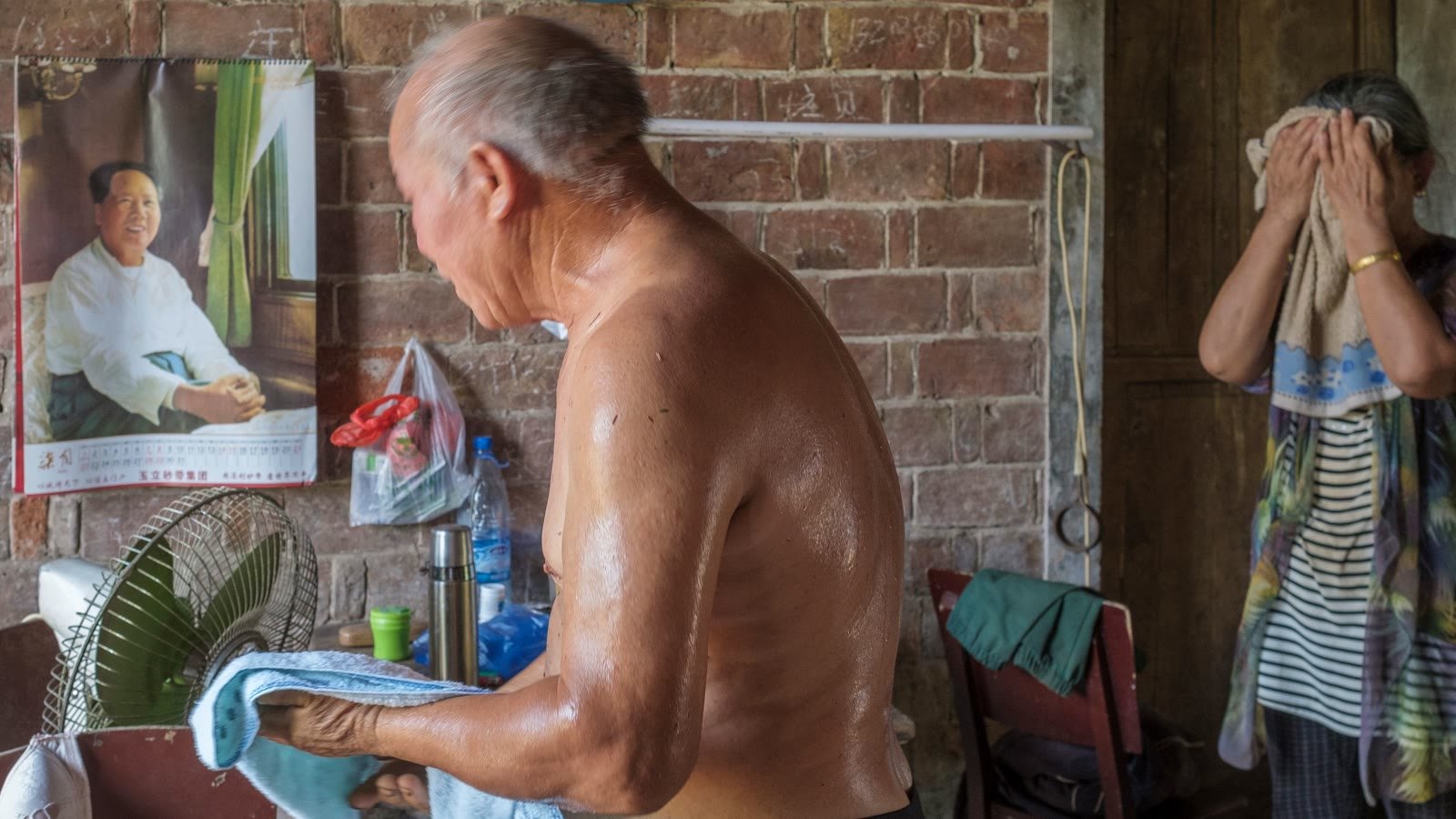 Older couple cooling down indoors beside an electric fan