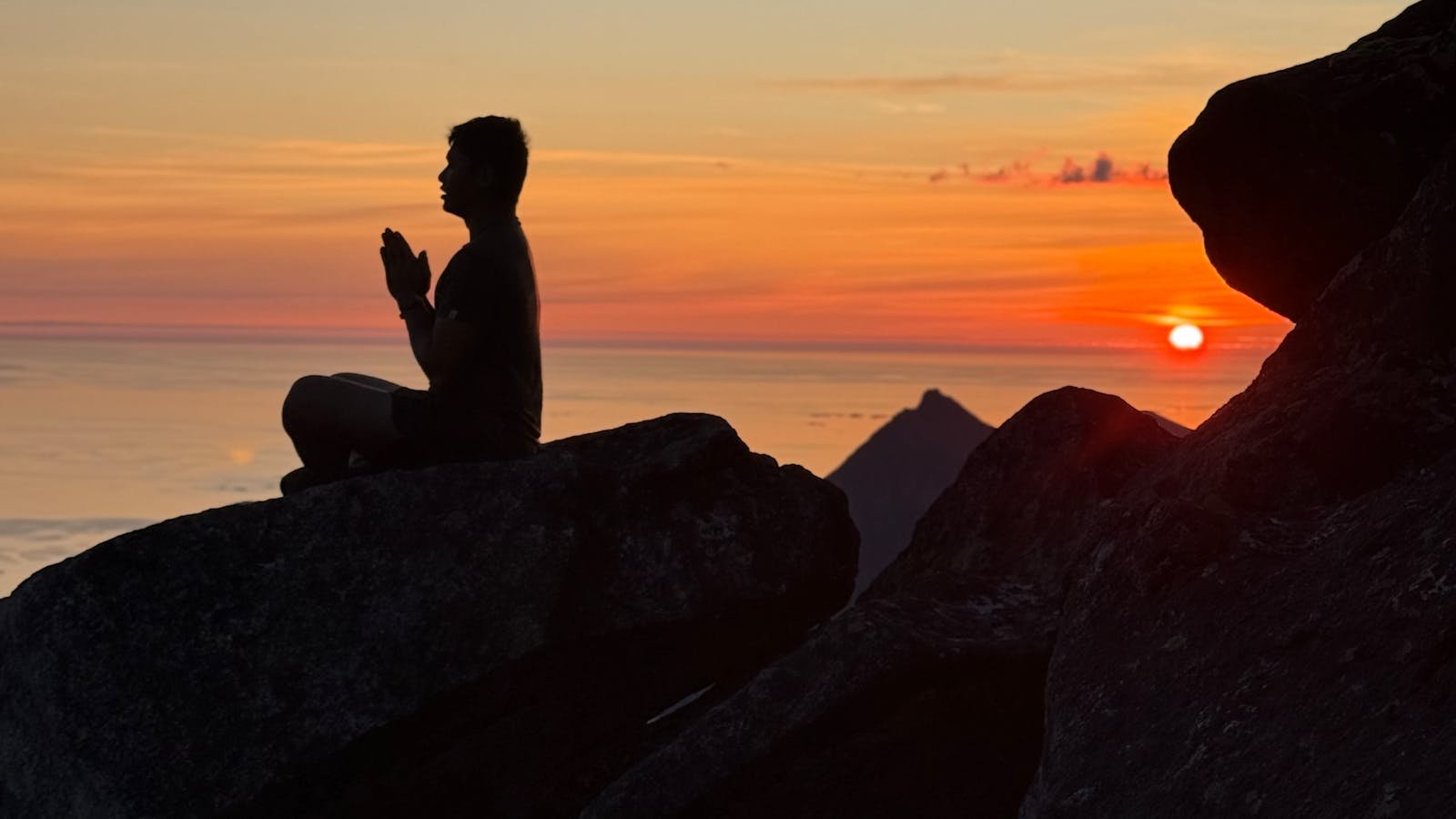 A person meditating on a mountain at sunset