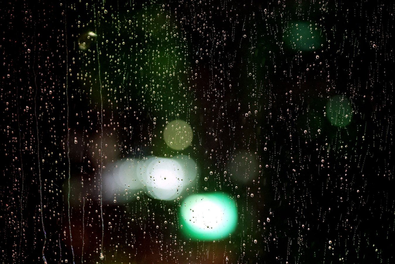 Raindrops on a window with blurred city lights in the background at night