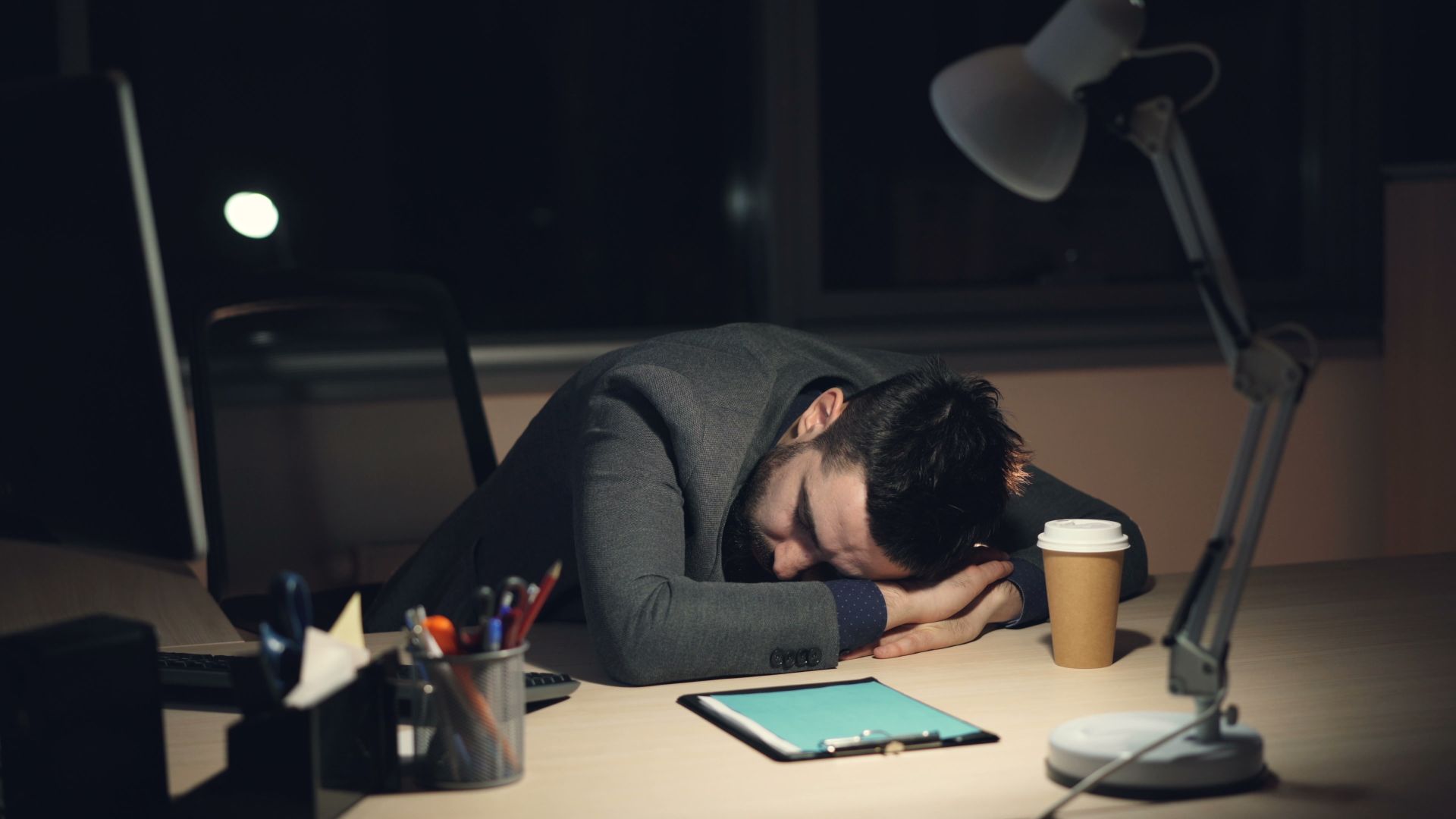 A tired shift worker resting their head on a desk late at night