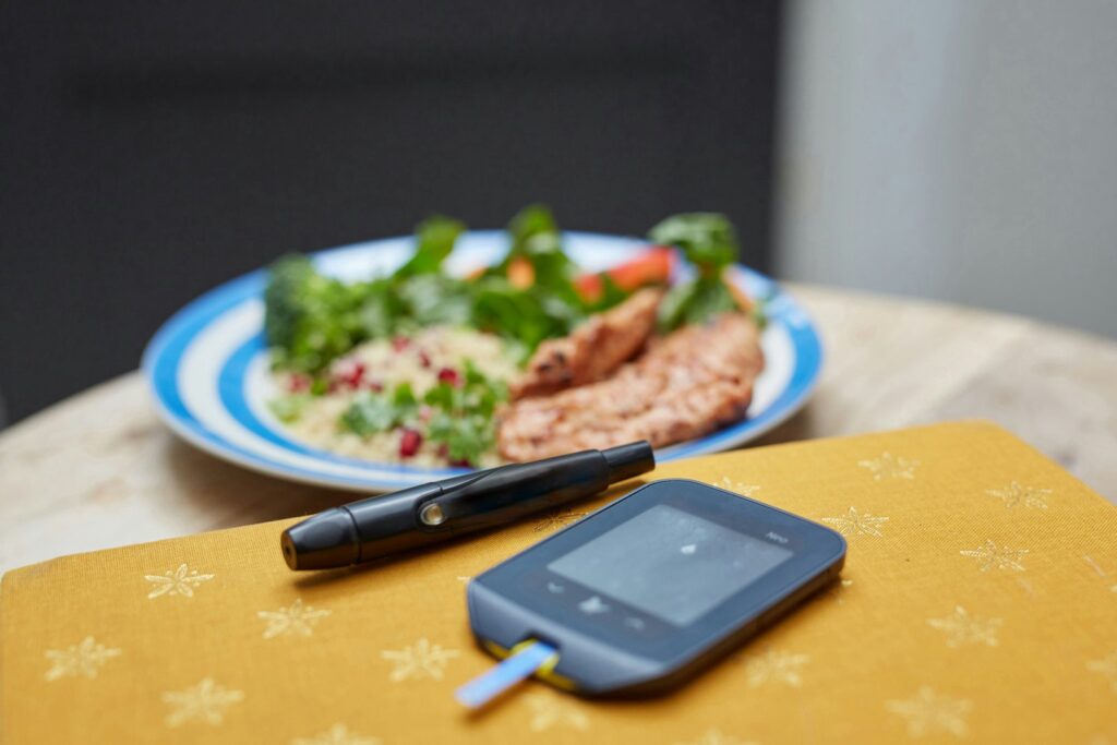 A glucometer and lancet on a table beside a plate of food