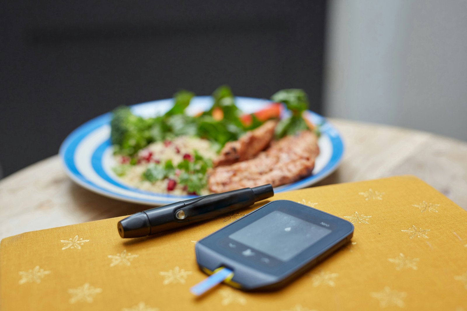 A glucometer and lancet on a table beside a plate of food
