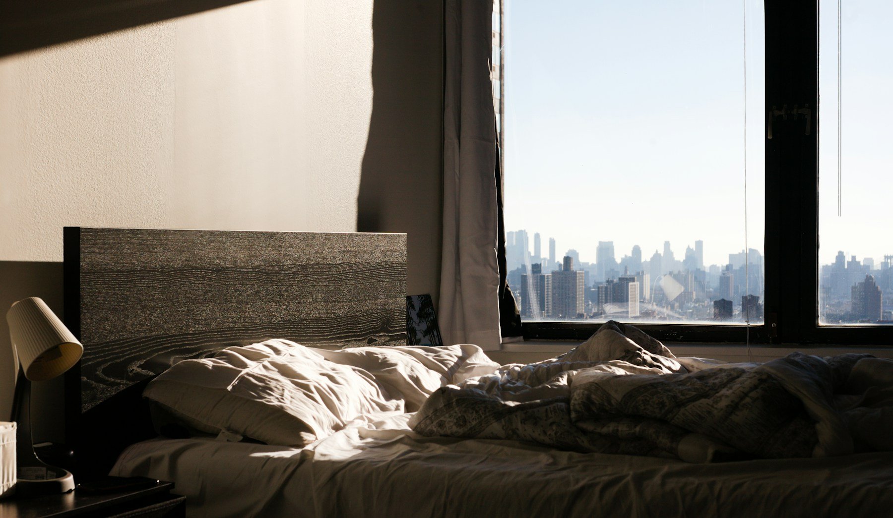 Sunlit unmade bed in a bedroom with a city view