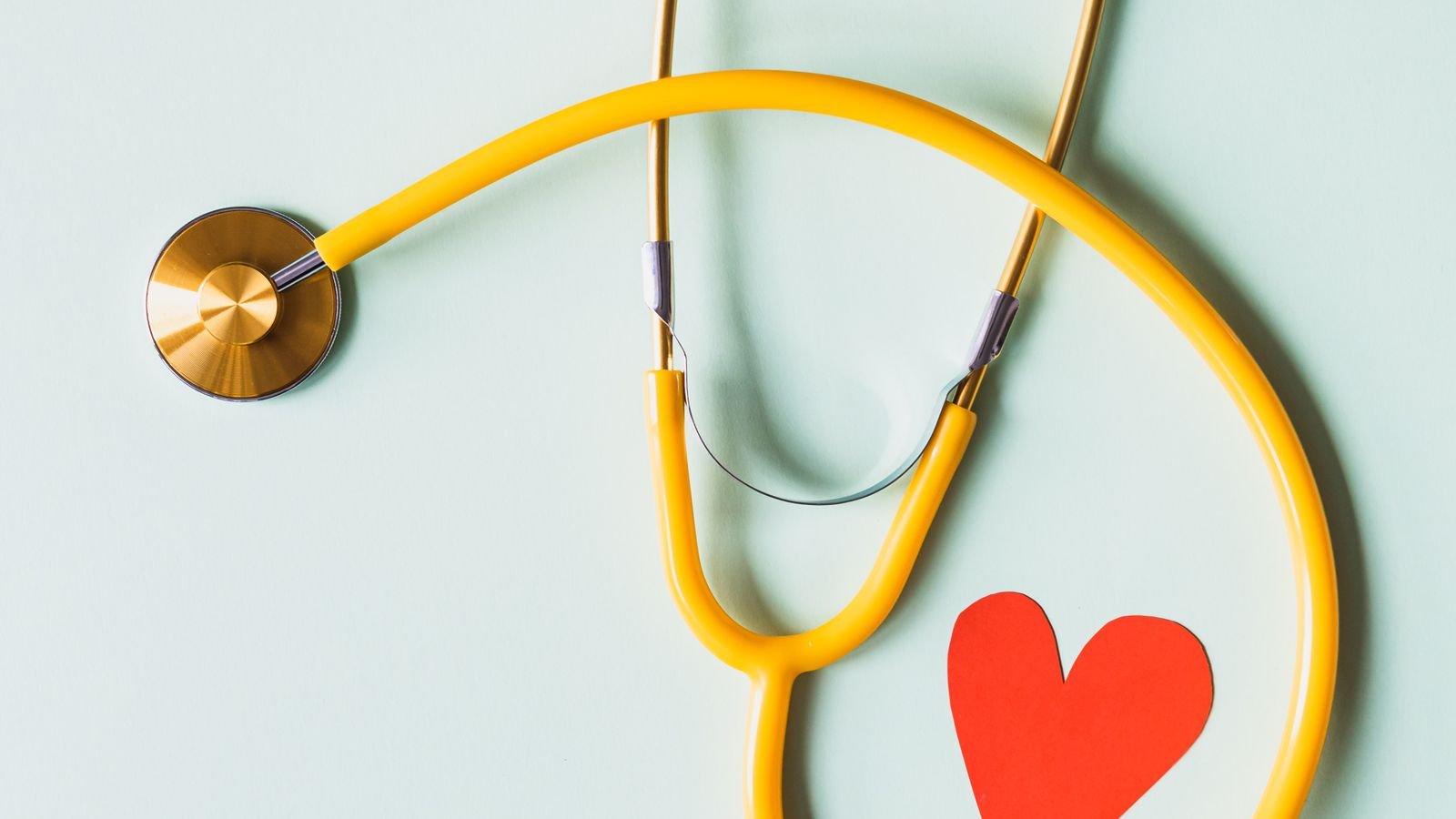 Medical stethoscope beside a red paper heart on a pale surface