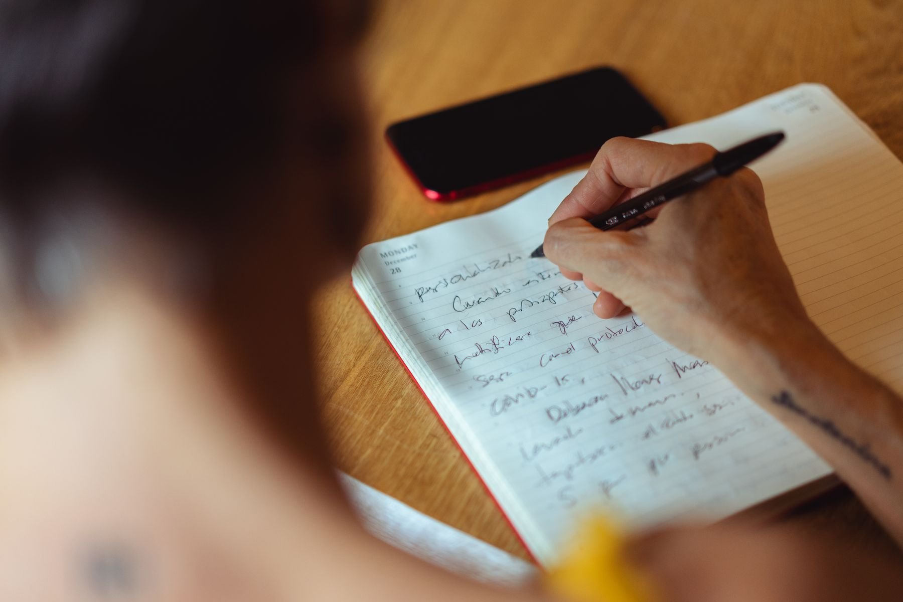 A person writing in a notebook at a wooden desk