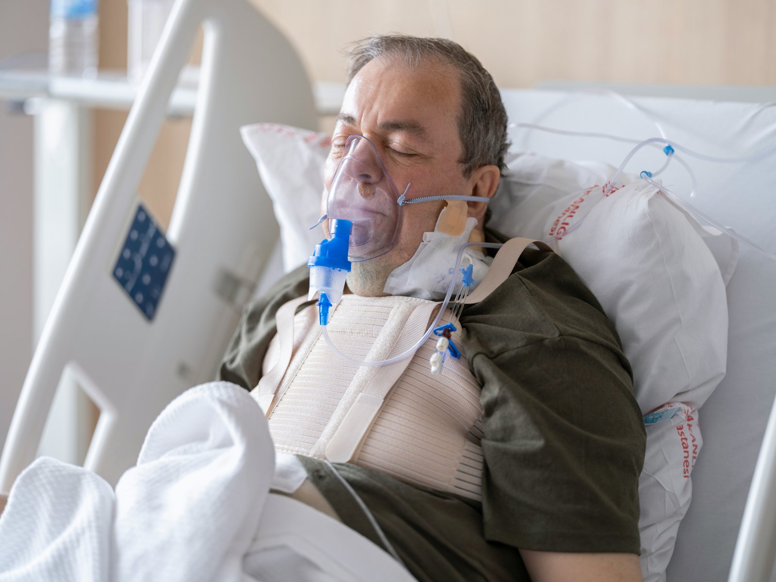 A man resting in a hospital bed with a breathing mask, used to illustrate sleep apnoea treatment comfort.