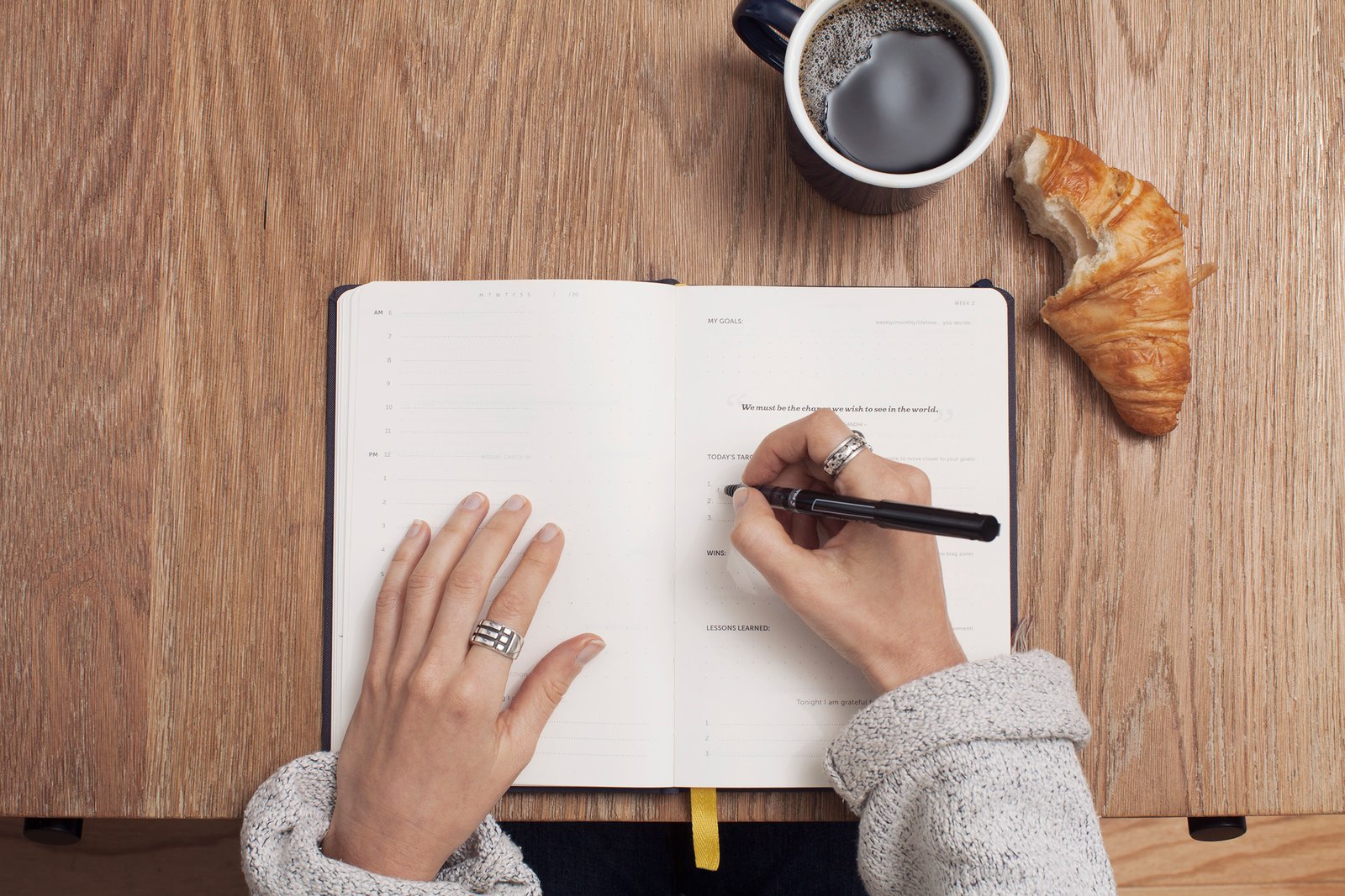 Person writing in a journal with pen and planner on a desk