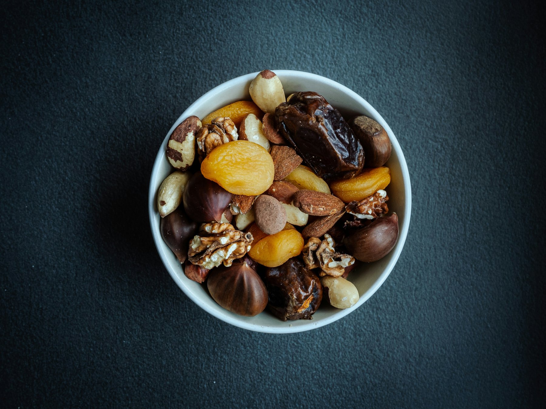 A bowl of mixed nuts and dried fruit on a dark table