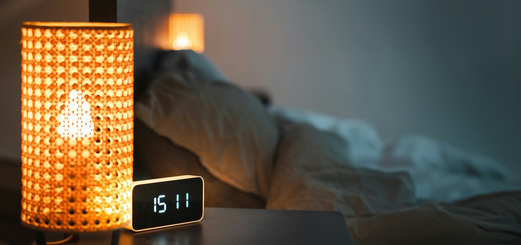 A bedside clock and lamp in a dim bedroom at night