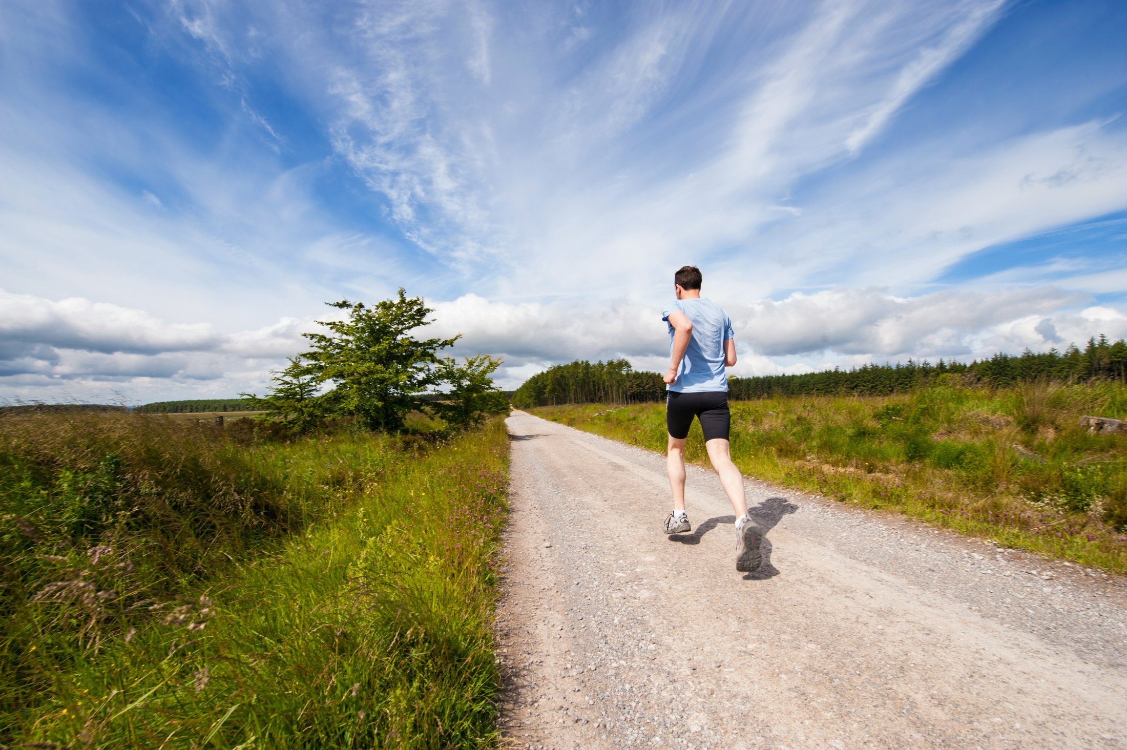Man running on a road near a grass field