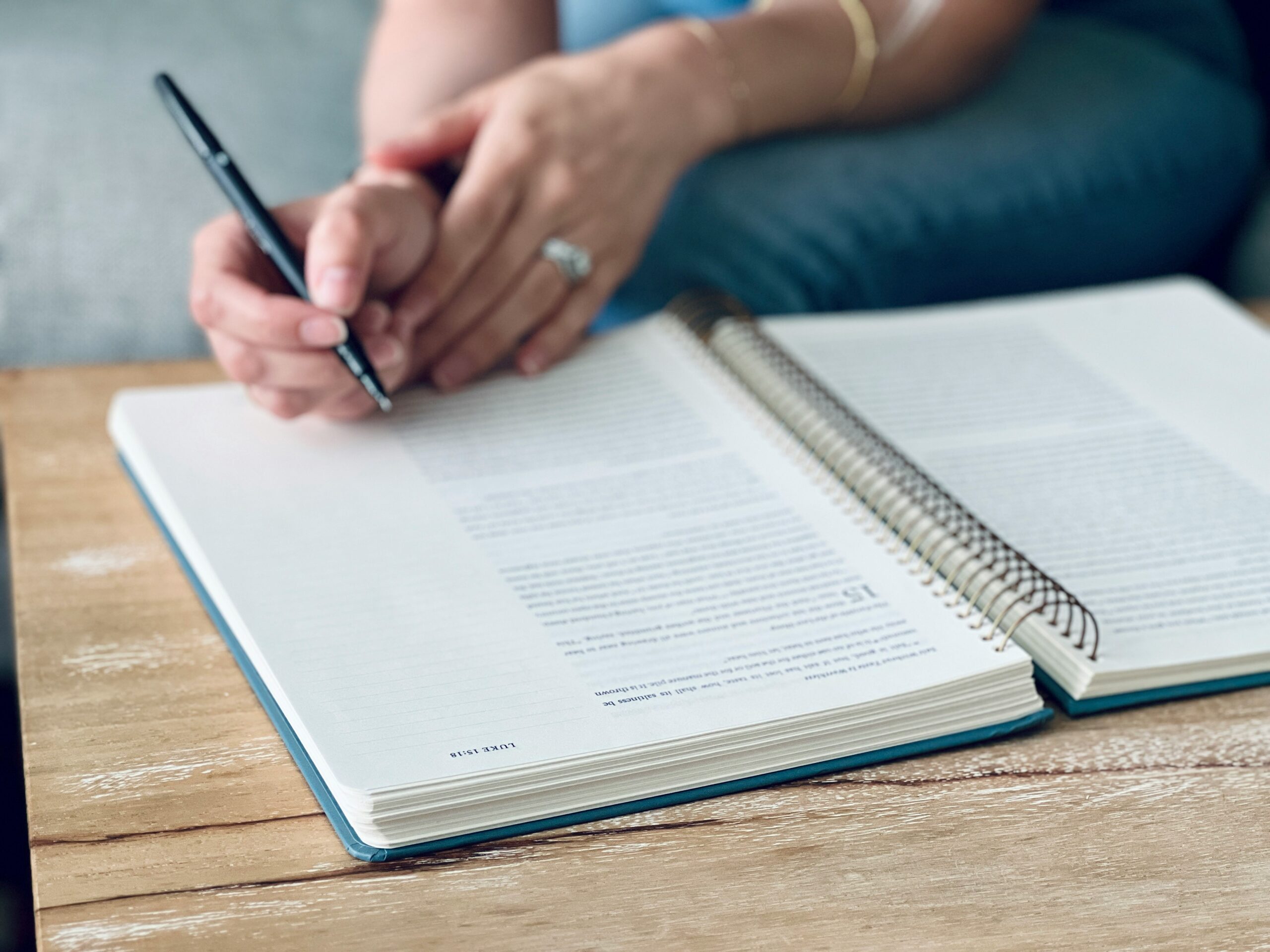A person holding a pen above an open notebook on a wooden table