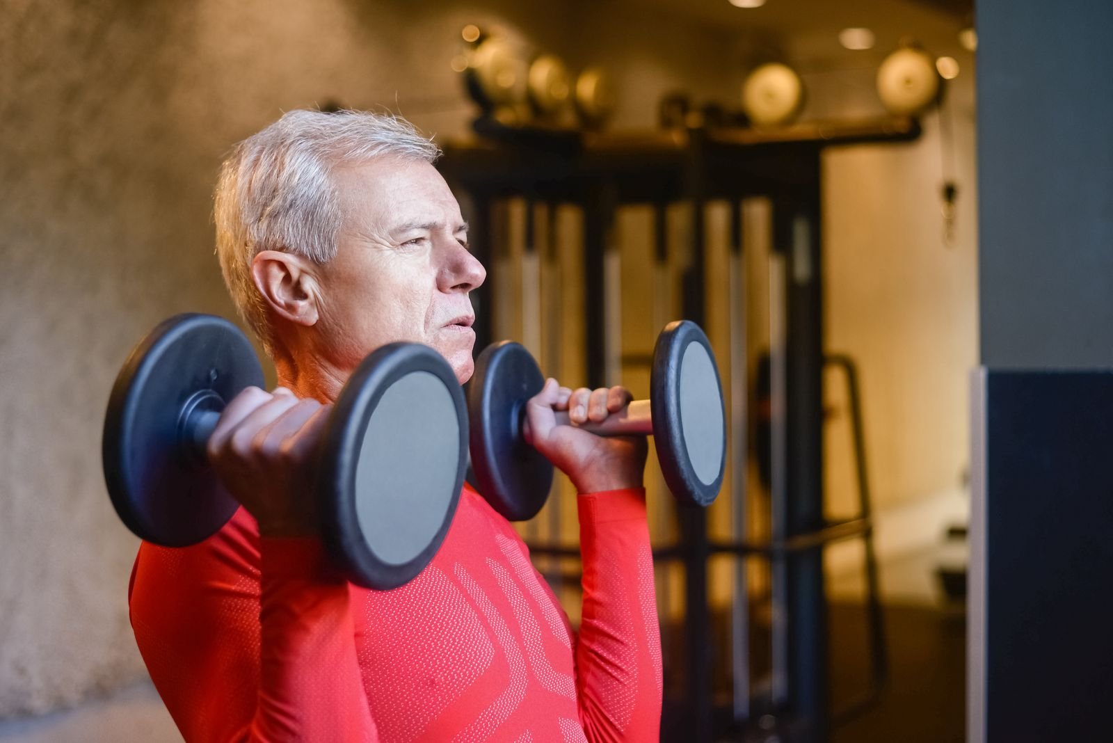 Older adult performing a controlled strength exercise with dumbbells in a gym