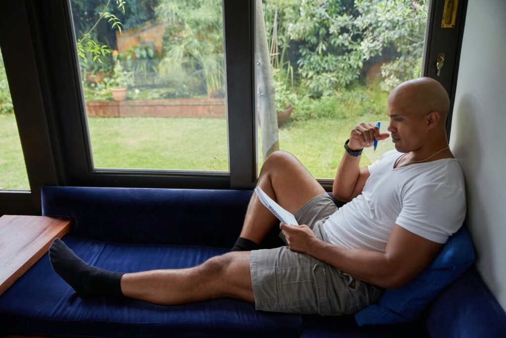 A man sitting on a blue couch looking out of a window