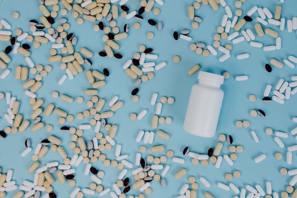 White supplement bottle and assorted pills on a blue surface