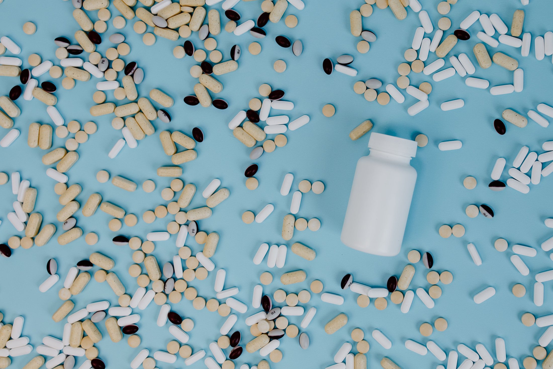 White supplement bottle and assorted pills on a blue surface
