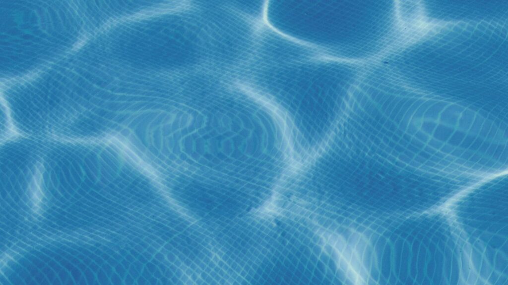 Sunlight ripples across blue swimming-pool water.