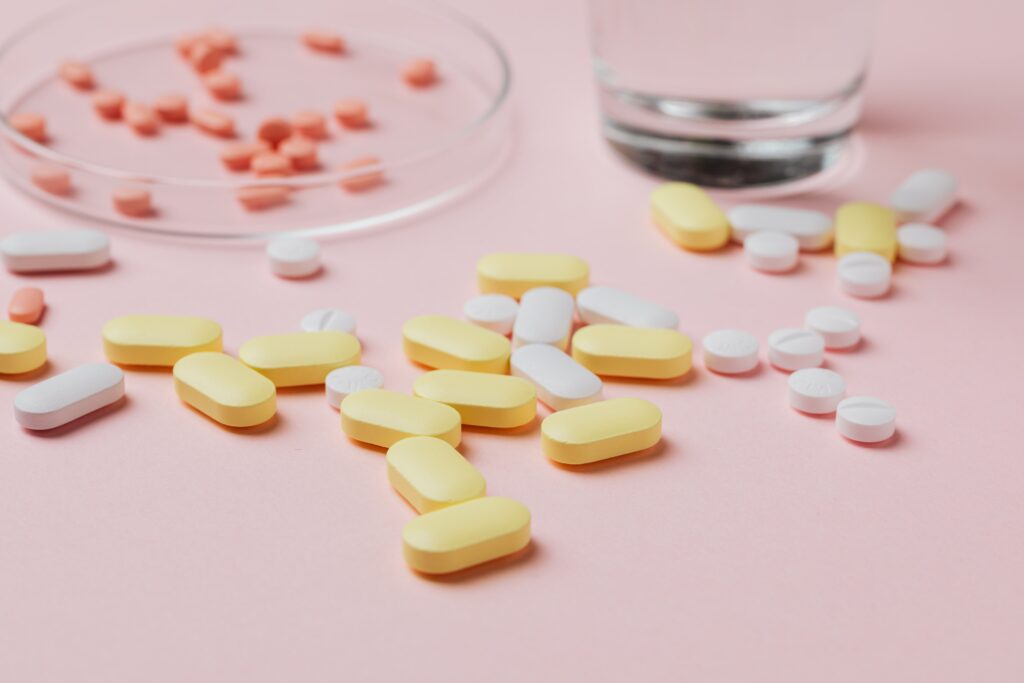 Assorted tablets beside a glass of water on a pink surface; illustrative image
